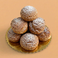 Stack of powdered sugar-covered pastries on a gold plate with a beige background