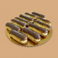 Eclairs with chocolate topping on a gold tray against a beige background